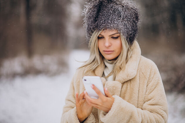 美丽穿着冬衣的女人走在满是雪的公园里打电话寒冷温暖的衣服探索