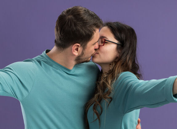 休闲一对穿着蓝色休闲服的年轻美男和一对热恋中的情侣站在紫色的墙上 幸福地亲吻着亲吻站立年轻