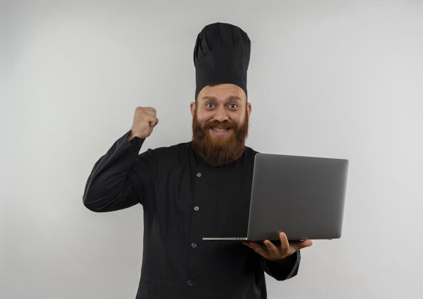 提高快乐的年轻帅哥厨师身着厨师制服 手持笔记本电脑 举起拳头孤立在白墙上烹饪拳头英俊
