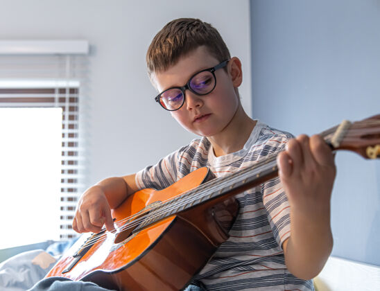 旋律戴眼镜的可爱男孩在家学弹古典吉他吉他手室内播放器