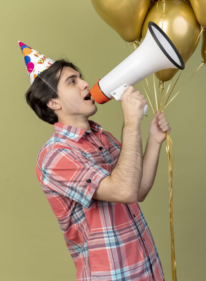 侧身自信英俊的白种人戴着生日帽站在一边拿着氦气球 对着扩音器讲话生日举行信心