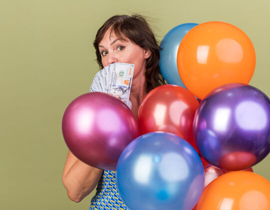 庆祝中年妇女一堆五颜六色的气球拿着现金站在绿色的墙上欢庆生日派对中间生日束