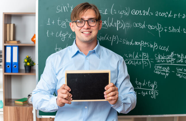 老师年轻的男老师戴着眼镜 拿着小黑板 面带微笑 自信地站在教室里的数学公式黑板旁眼镜公式数学