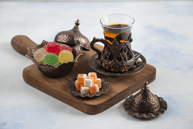 美味木板上有五颜六色的糖果和香喷喷的茶传统茶壶玻璃