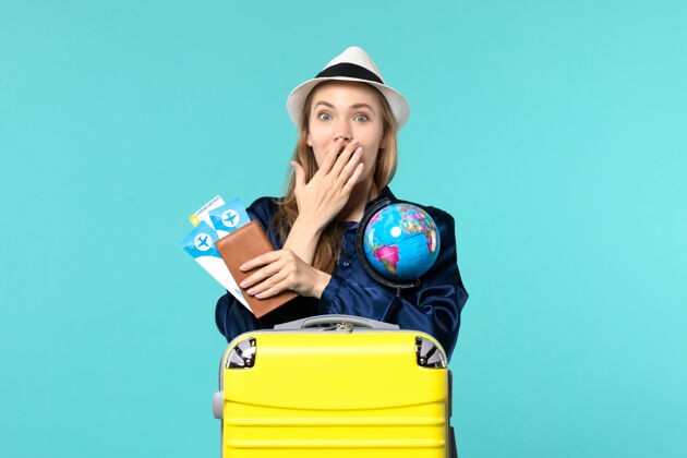 年轻女子前视图年轻女子拿着机票和地球仪在淡蓝色背景的飞机上航行海上度假之旅航程微笑地球仪