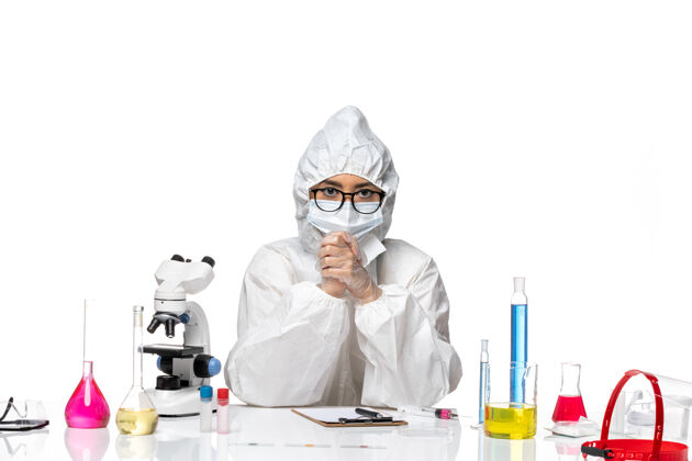 病毒前视图穿着特殊防护服的年轻女化学家正坐在白色背景的实验室里 科维化学病毒健康医生化学实验室外套