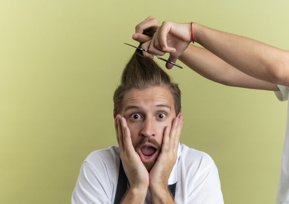 害怕年轻英俊的理发师惊讶地把手放在脸上 害怕把所有的头发都剪掉 孤立在橄榄绿的墙上剪人表情
