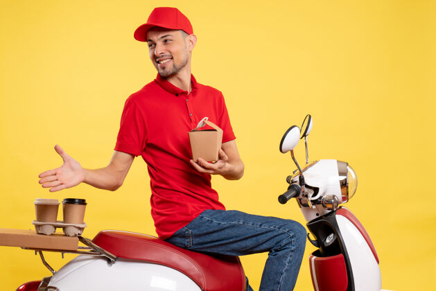 服务正面图身穿红色制服的年轻男性快递员 黄色背景上几乎没有送货食品红色送货摩托车