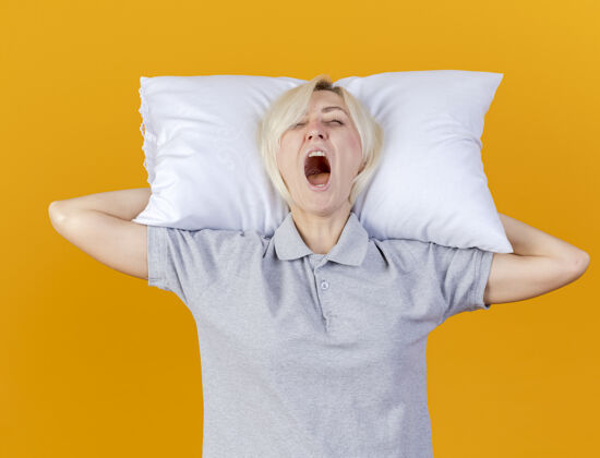 人昏昏欲睡的年轻金发病女人打着哈欠 把头枕在橘色的墙上抱着脸年轻