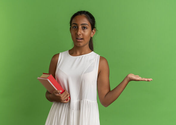 壁板看着镜头 年轻的女学生拿着笔记本 用手指着旁边的书绿色背景年轻