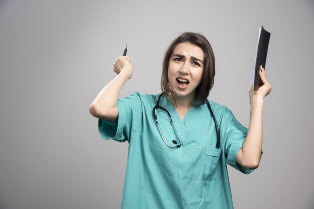 妇女愤怒的医生拿着剪贴板和笔在灰色背景上高质量的照片工作女性成人