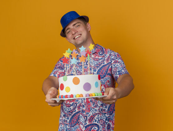 橙色微笑着的年轻人戴着蓝色的帽子拿着蛋糕孤立在橙色年轻人拿着戴着