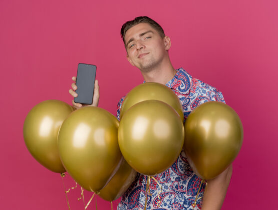 派对高兴的年轻人穿着五颜六色的衬衫站在气球和手持电话孤立的粉红色气球中间小伙子