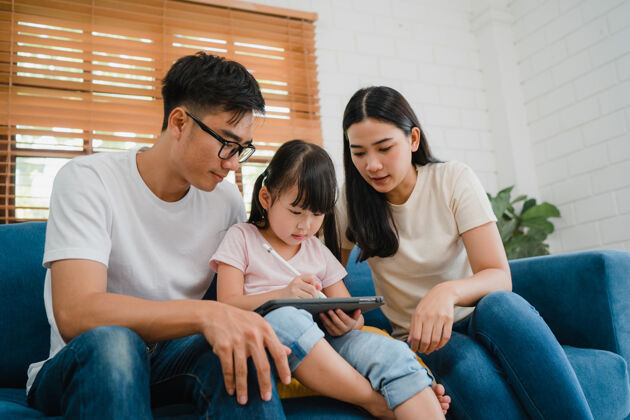 家庭学校快乐亚洲家庭爸爸 妈妈和女儿用电脑平板电脑技术坐在客厅的沙发上日本人手表父母