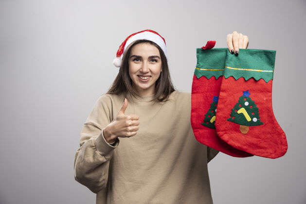 圣诞老人戴着圣诞老人帽子的小女孩竖起大拇指 手里拿着两只圣诞袜子欢呼惊人手势