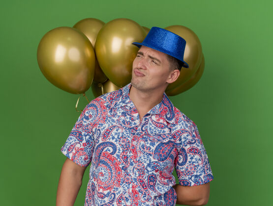 派对一个戴着蓝帽子的年轻人站在绿色的气球前绿色穿小伙子