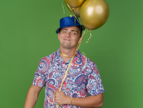 脖子高兴的年轻人戴着蓝帽子拿着气球围着脖子上的绿色隔离绿色抱着年轻人