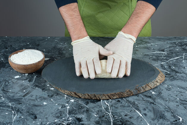 揉捏男人戴着手套在大理石桌上做面团面包糕点手工制作