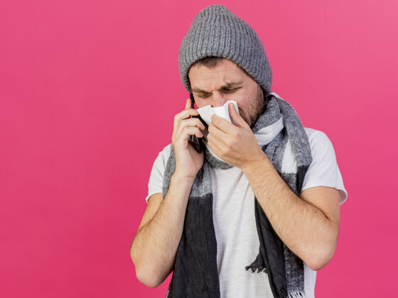 湿巾戴着带围巾的冬帽的年轻病夫在电话里讲话 用隔离在粉色上的餐巾擦鼻子电话餐巾帽子