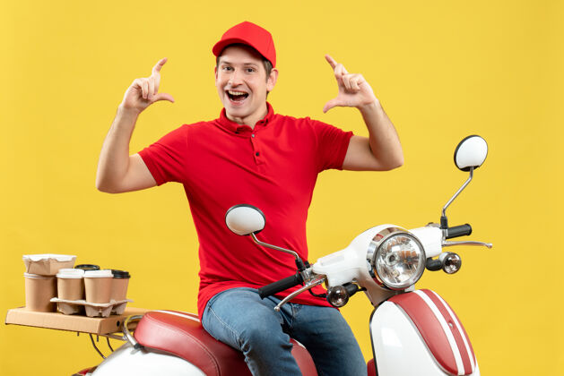 摩托车正面图是一个微笑的年轻人 穿着红色上衣 戴着帽子 在黄色背景下发订单车辆订购帽子