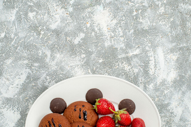 底部上半部分查看巧克力饼干草莓和圆形巧克力在白色椭圆形盘子底部的灰白色地面水果食品草莓