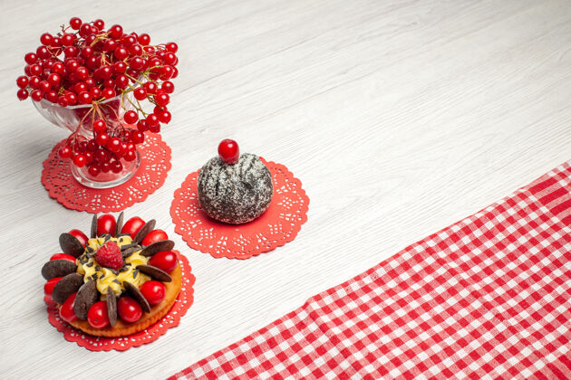 蛋糕上图：红色椭圆形蕾丝桌布上的水晶玻璃浆果蛋糕和可可蛋糕中的红醋栗 白色木桌上的红白格子桌布水晶可可玻璃