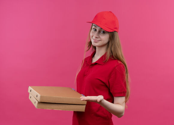 盒子穿着红色制服的年轻送货女孩高兴地拿着包裹 在孤立的粉色空间里空手而归请制服年轻