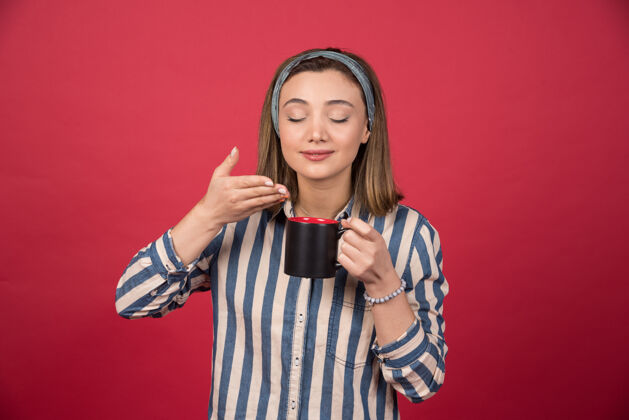 乐趣快乐的女人在红墙上闻到咖啡的香味咖啡马克杯模型