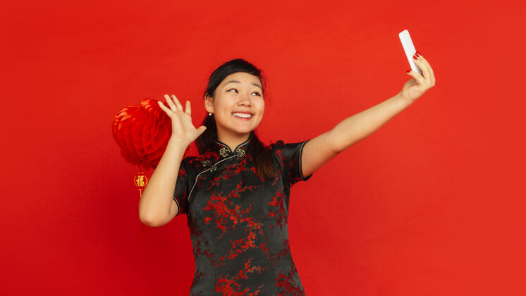 手2020年中国新年红色背景上的亚洲少女肖像穿着传统服装的女模特看起来很开心 带着装饰自拍庆祝 节日 情感传单普通话欢呼旗袍