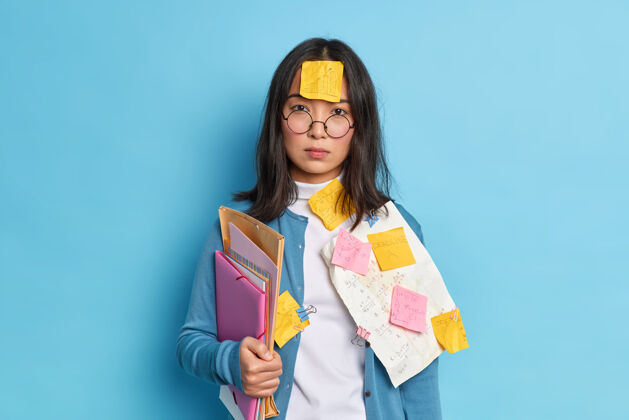 文件严肃的黑发亚洲女人额头贴着贴纸忙着做文书工作准备财务报告戴着圆眼镜休闲套头衫看起来很聪明女人眼镜姿势
