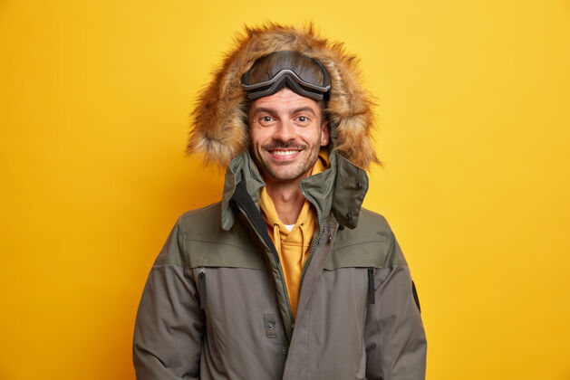 舒适快乐的欧洲男人穿着夹克 头戴皮帽 感觉温暖舒适 在冬天享受最喜欢的季节 微笑着 快乐地戴着滑板护目镜 积极地休息外套积极人