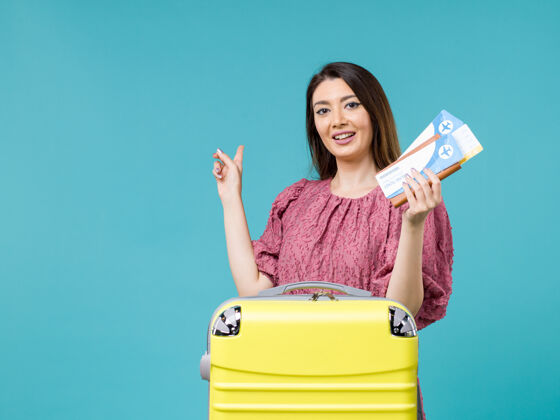 票前景度假中的女性手持浅蓝色背景的机票旅行暑期旅行女性海上度假表演微笑前面