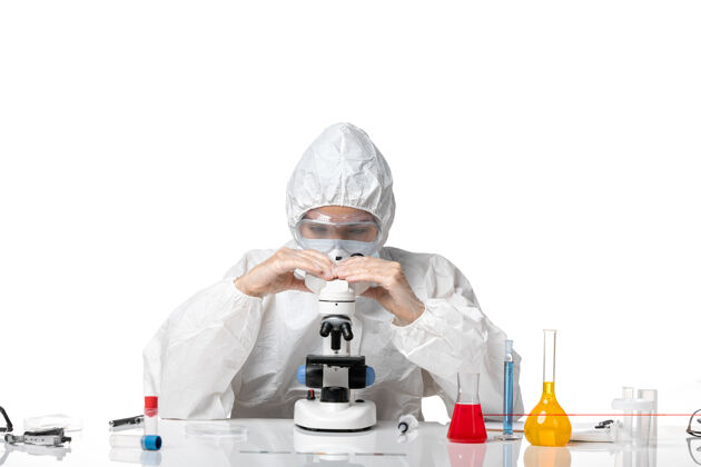 正面正面图女医生穿着防护服 戴着口罩 用显微镜观察白色背景病毒大流行时的健康状况化学专业防护
