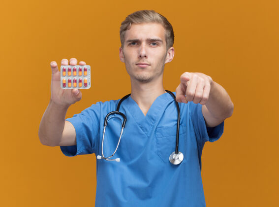 医生自信的年轻男医生 穿着医生制服 手持听诊器 在橙色的墙上显示你的手势自信姿势感觉