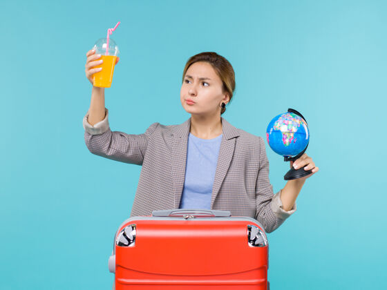 观点正面图：度假中的女性手持新鲜果汁和地球仪在蓝色背景下进行海上旅行度假微笑人女人
