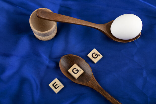天然一个生鸡蛋 蓝色棉缎布上有木制勺子和木制字母勺子新鲜有机