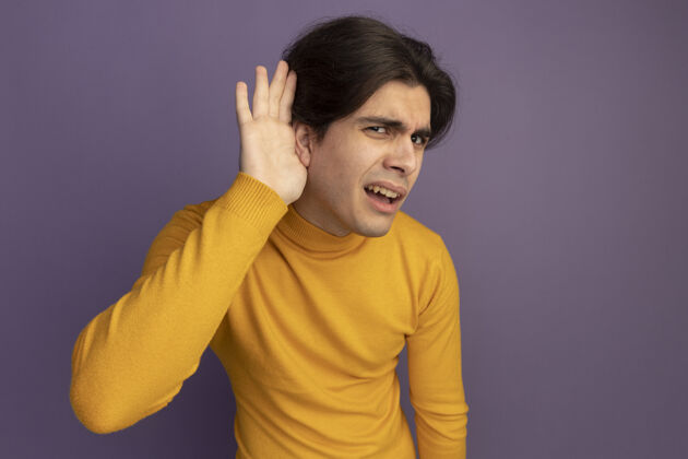 穿迷茫的年轻帅哥穿着黄色高领毛衣 在紫色的墙上显示出一种孤立的倾听姿态高领毛衣手势困惑