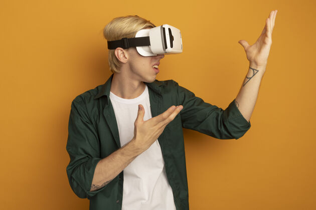 游戏困惑的年轻金发男子穿着绿色t恤和虚拟现实耳机点 双手放在一边技术虚拟现实耳机困惑