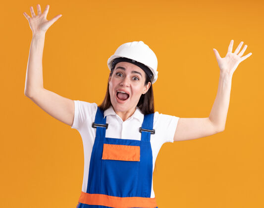 举起来一个穿着制服的年轻建筑工人被吓坏了 她举起双手孤立在橙色的墙上害怕女人制服