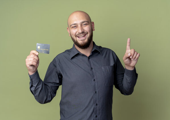 男人快乐的年轻秃头呼叫中心男子举行信用卡和提高手指孤立在橄榄绿手指信用中心