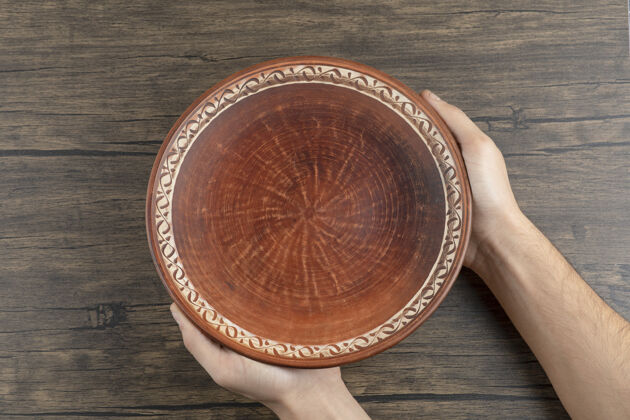 盘子的顶视图：一只手拿着一个空的棕色盘子放在木桌上白的胳膊的发亮的