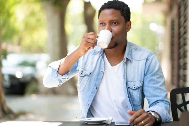 时间非裔美国人坐在户外的咖啡馆里享受和喝咖啡杯子欢呼桌子