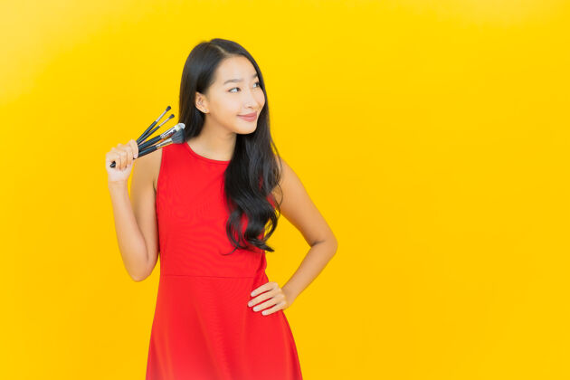 魅力用化妆刷在黄色墙上描绘美丽的亚洲年轻女子魅力黑发画笔