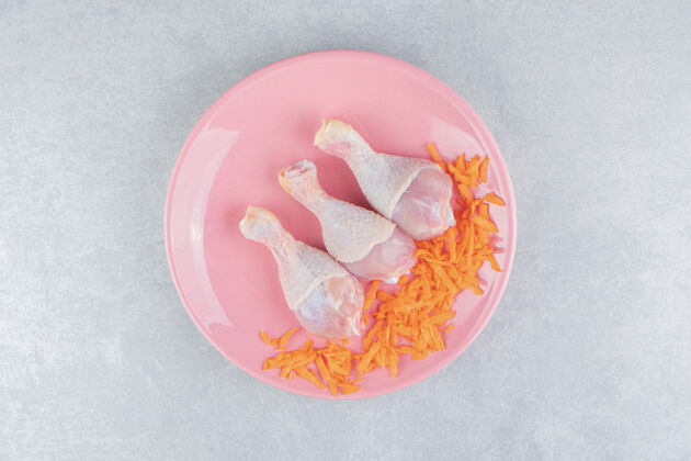 家禽把胡萝卜和鸡腿放在盘子里 放在大理石表面美味感恩可口