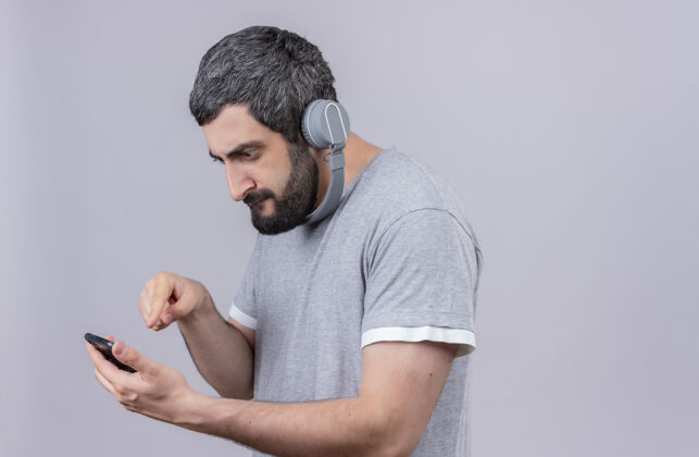 手机年轻英俊的白人男子戴着耳机 看着和使用他的手机 白色背景下的复制空间隔离穿着耳机手机