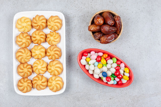 甜点在大理石背景的盘子上 一碗碗的枣子和糖果旁边放着一捆酥脆的饼干高质量的照片零食垃圾食品水果