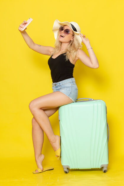 年轻正面图度假中的年轻女性坐在包上自拍黄色墙壁上的彩色女孩女性旅行海上之旅自拍成人颜色