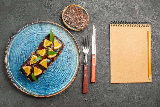 饼干用叉子和刀子在黑色桌子上的笔记本旁水平观看美味的蛋糕和饼干刀叉子财务