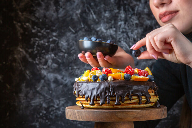 前面正面图美味的巧克力蛋糕被女性用水果装饰在黑暗的墙上公园甜点蛋糕