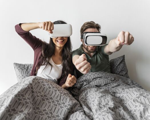 休闲笑脸女人和男人在床上使用虚拟现实耳机虚拟现实眼镜享受水平